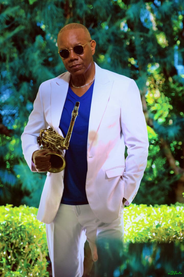 A man in a white suit holding a saxophone.