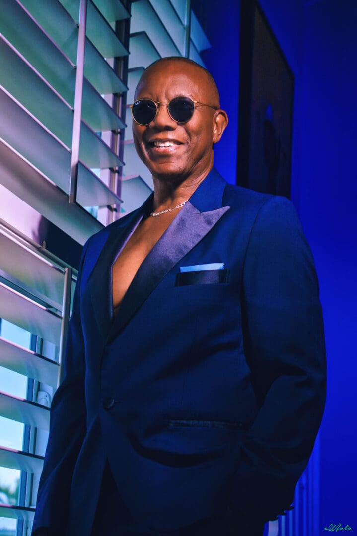 A man in a blue suit and sunglasses is posing for a photo.