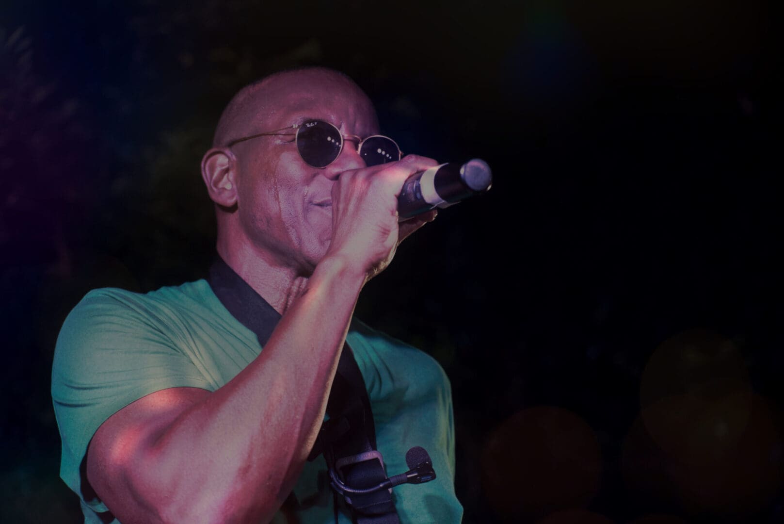 A man in sunglasses singing into a microphone.
